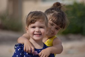 Two young girls are hugging each other outside.