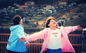 Two girls holding hands and standing on a bridge.