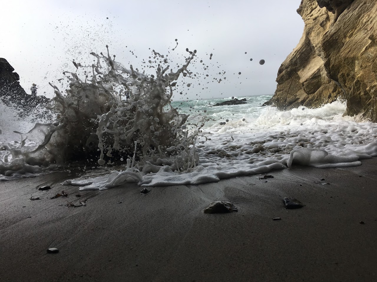 A wave crashes on the beach as a boat approaches.