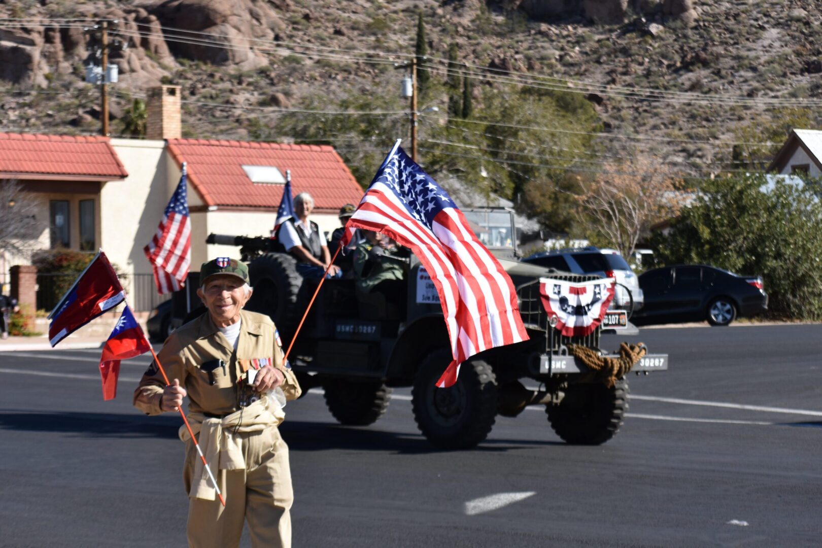 A man in uniform holding flags while standing next to an army vehicle.