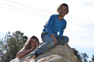 A boy and girl sitting on top of a rock.