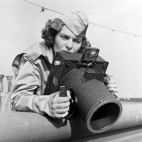 A woman in uniform holding an old camera.