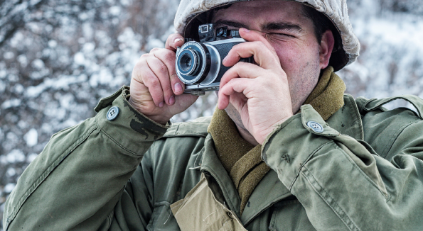 A man in military clothing taking a picture with his camera.