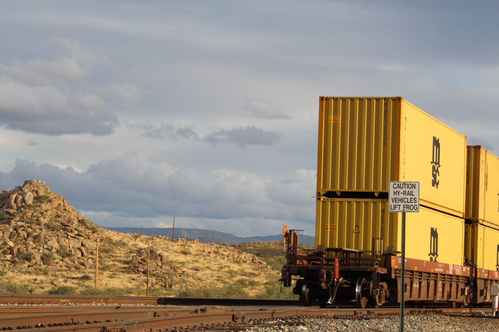 A yellow truck parked on the side of train tracks.