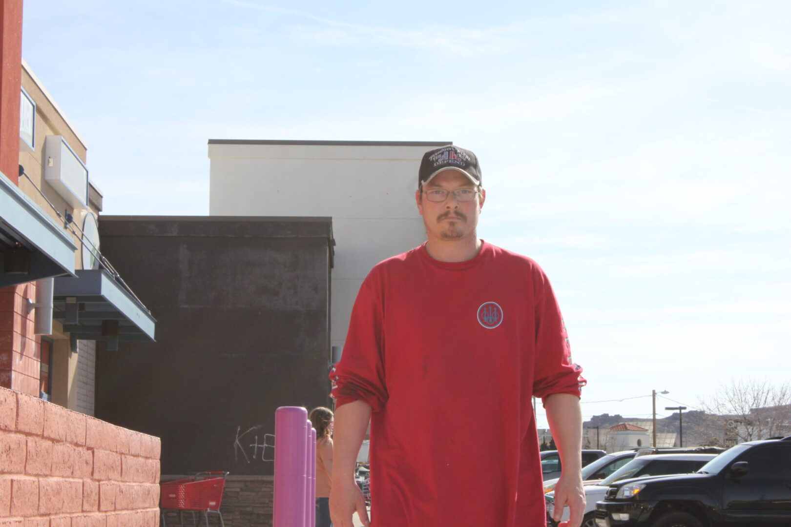 A man in red shirt standing next to some cars.