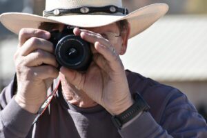 A man in a cowboy hat taking a picture with his camera.