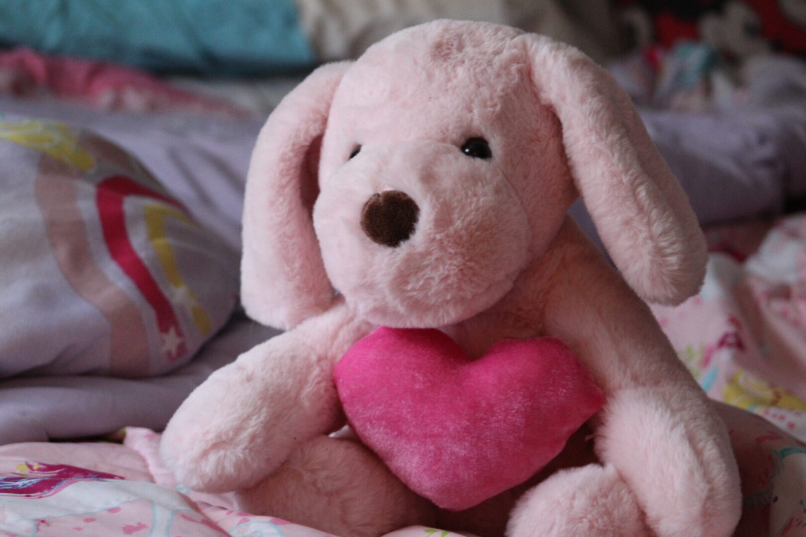 A pink stuffed animal holding a heart in its mouth.